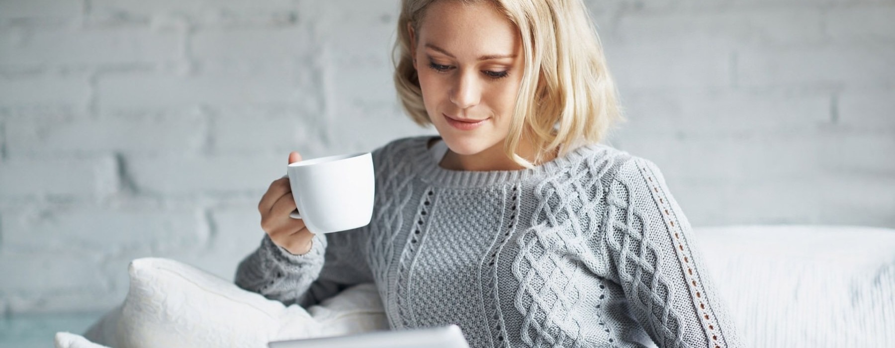 a woman holding a coffee cup looking and a tablet